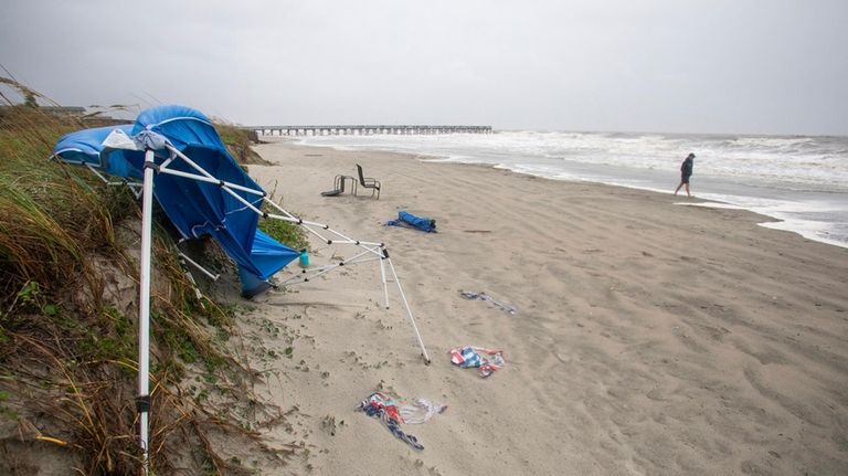 A person walks on a windy and rainy beach as...