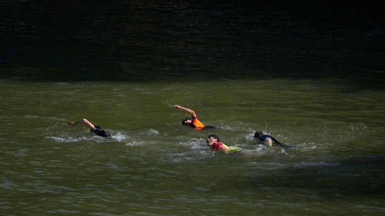 Paris Mayor Anne Hidalgo, center, in the background, swims in...