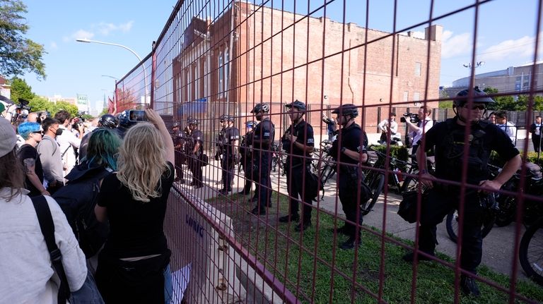 Police walk towards protesters who knock down a fence surrounding...