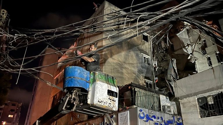 A man removes power cables near a destroyed building that...