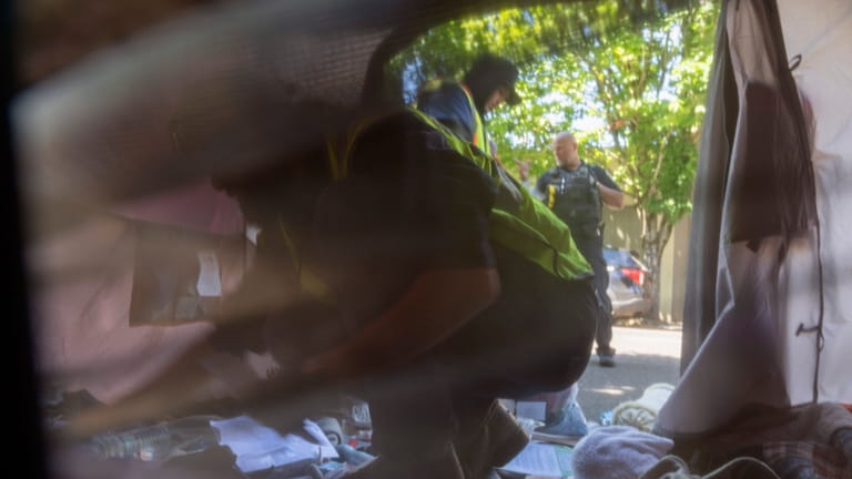 Workers remove contents from a tent after Portland police detained...