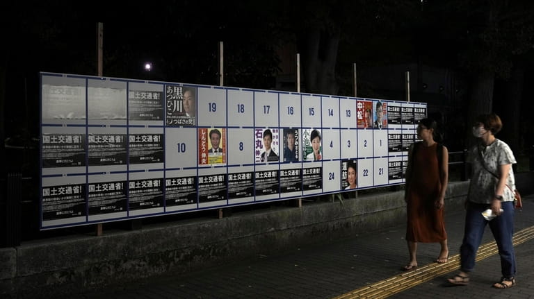 People walk by an election poster board for Tokyo gubernatorial...