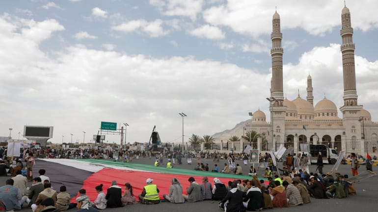 Houthi supporters sit in front of a giant Palestinian flag...