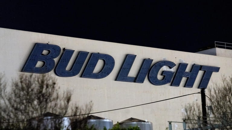 A Bud Light sign is illuminated by street lights on...
