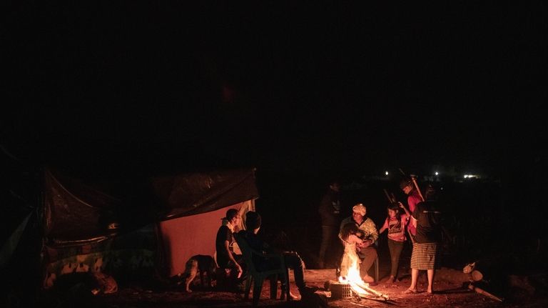 An Indigenous family sits around a fire next at a...