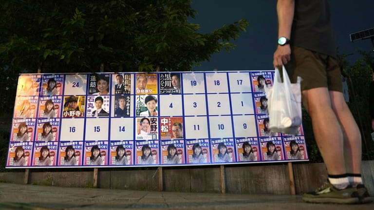 A person stands near an election poster board for Tokyo...