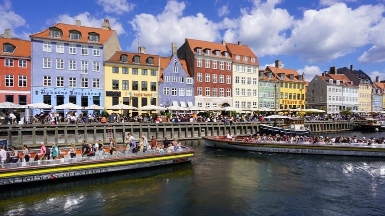 Sightseeing ferries navigate Copenhagen’s historic Nyhavn harbor area in Copenhagen,...