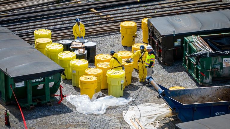 Workers with yellow containers holding the 55-gallon drums exhumed from...