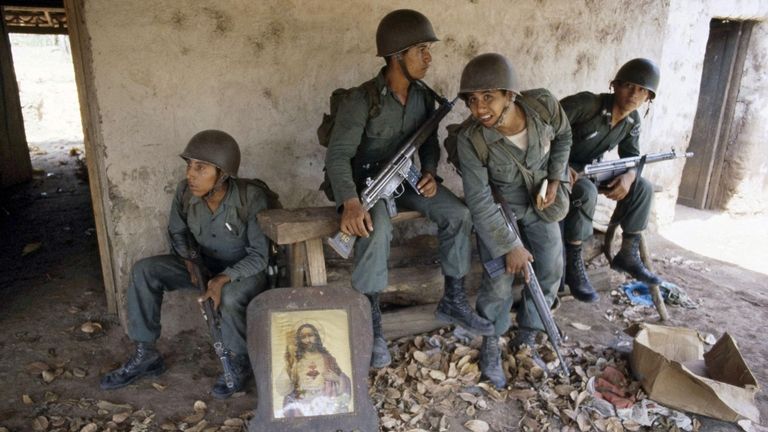 Salvadoran troops rest on the porch of a deserted farm...