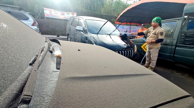 A disaster management agency official washes a car covered in...
