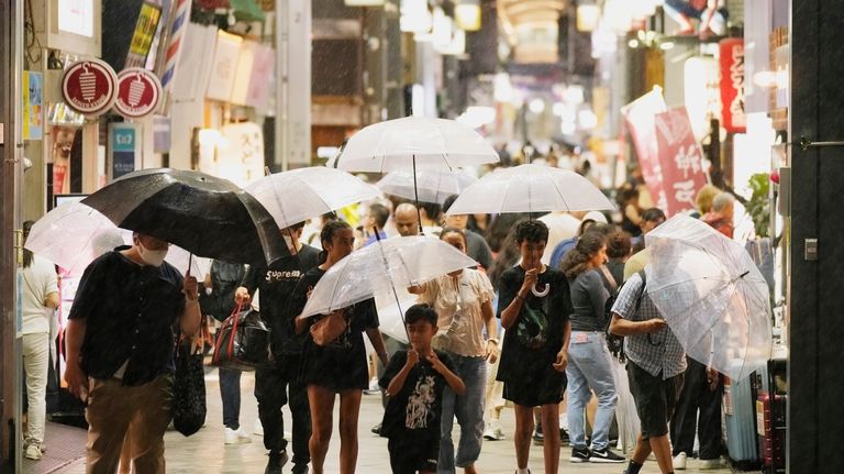 People use umbrellas as they walk through a shopping street...