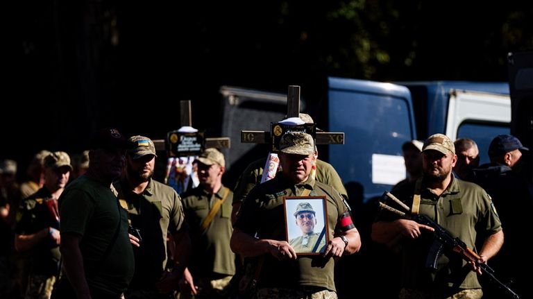 Ukrainian servicemen carry crosses and pictures of their comrades killed...