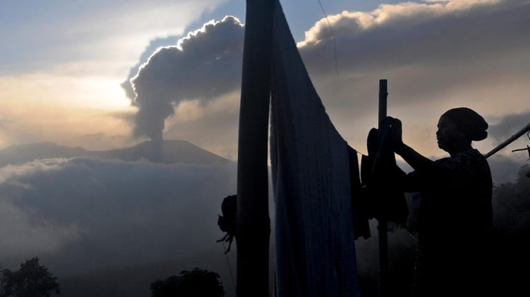 A woman hangs her laundry to dry as Mount Marapi...