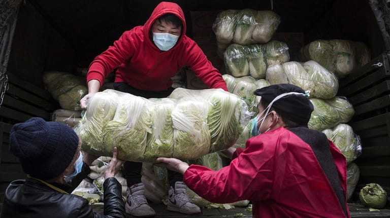 Employees wear protective masks Monday while carrying vegetables from trucks at...