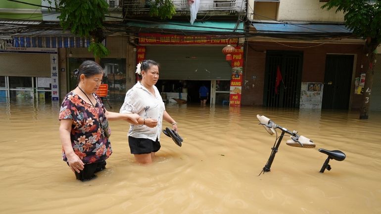 People wade in a flooded street in the aftermath of...