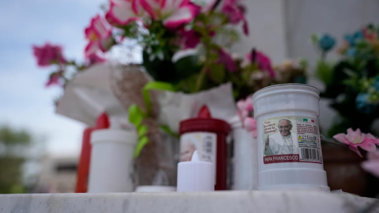 Candles with the image of Pope Francis are left at...