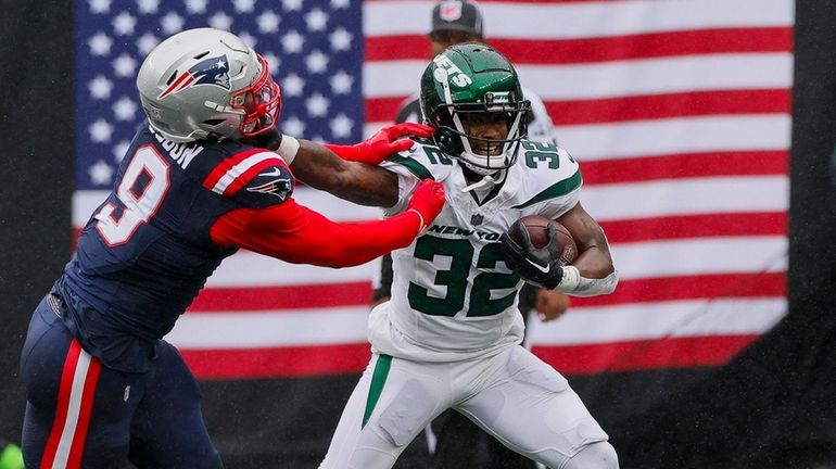 Jets running back Michael Carter (32) stiff arms New England...