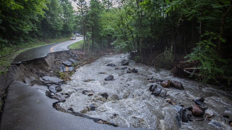 A river flows past a damaged road in the aftermath...