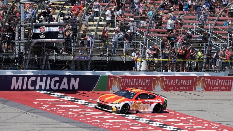 Tyler Reddick takes the checker flag after winning a NASCAR...