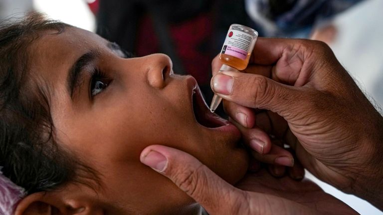 A health worker administers a polio vaccine to a child...