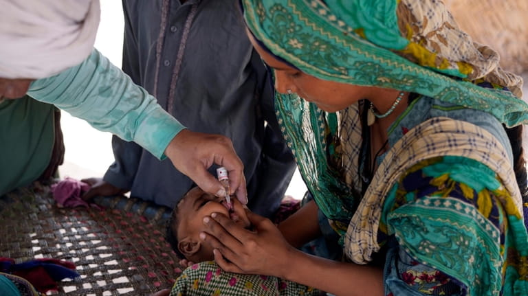 A health worker administers a polio vaccine to a child...