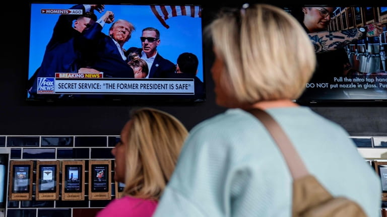 People watch news near the Fiserv Forum ahead of the...