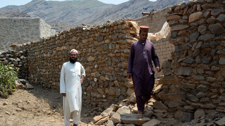 Local residents stand beside a wall damaged due to cross...