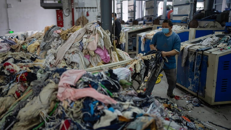 A worker feeds discarded textiles to a shredding machine at...