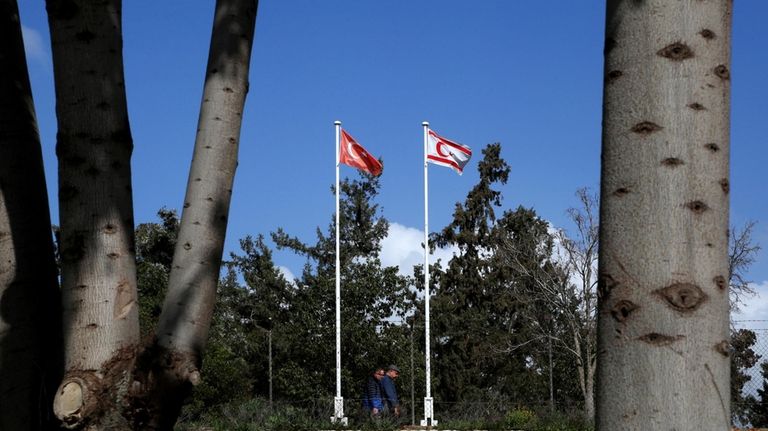 Men walk under a Turkish, left, and a Turkish Cypriot...