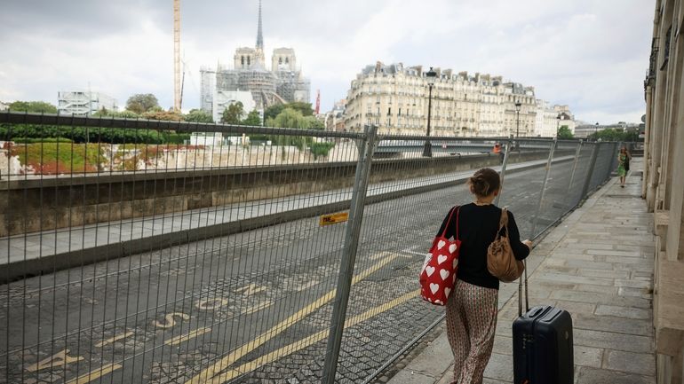 A woman pulls her luggage along fences of the security...