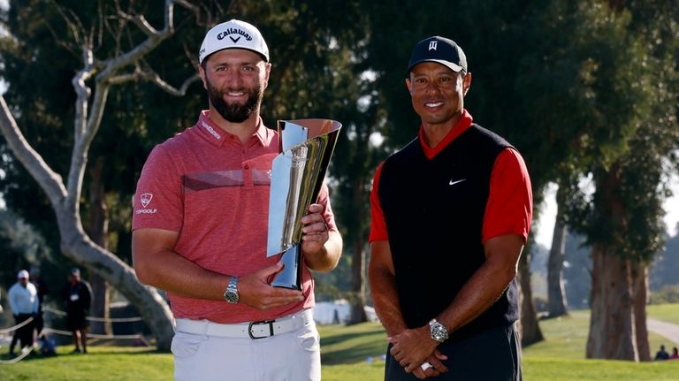 Jon Rahm, left, holds the winner's trophy next to Tiger...