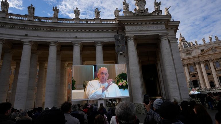 Pope Francis appears on a giant monitor set up in...