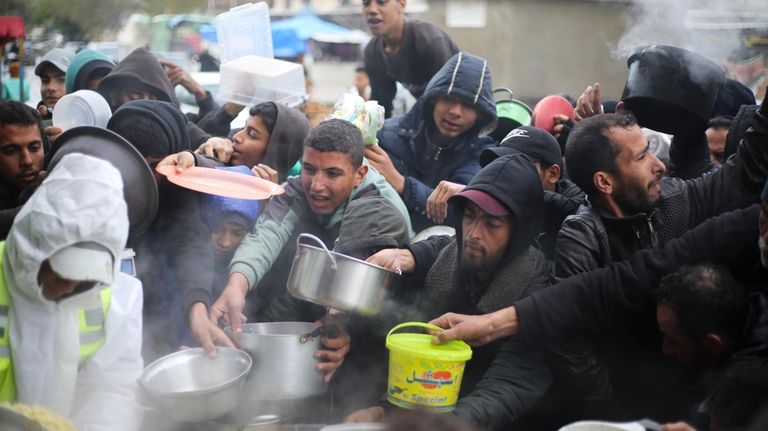 Palestinians line up for free food distribution during the ongoing...