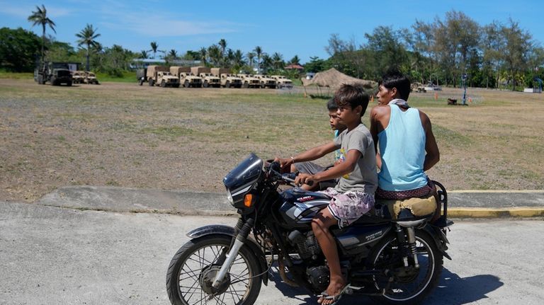 Filipinos drive their tricycle past U.S. military vehicles at the...