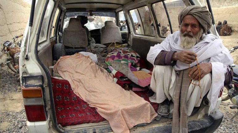 A man sits next to the covered body of a...