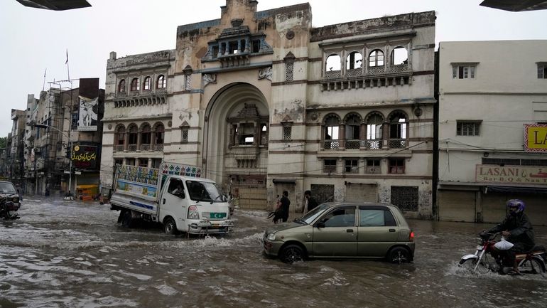 Motorcyclists and cars drive through a flooded road caused by...