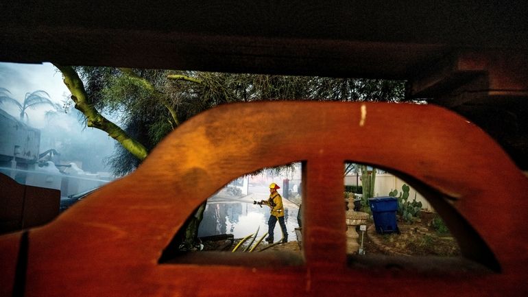 A firefighter hoses down the garage of Noel Piri's home...