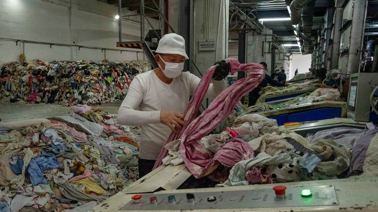 A worker feeds discarded textiles to a shredding machine at...