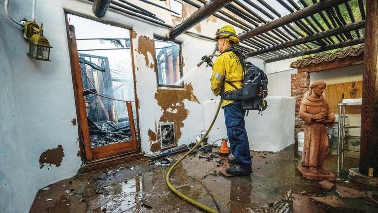 A firefighter hoses down hot spots at Noel Piri's home...