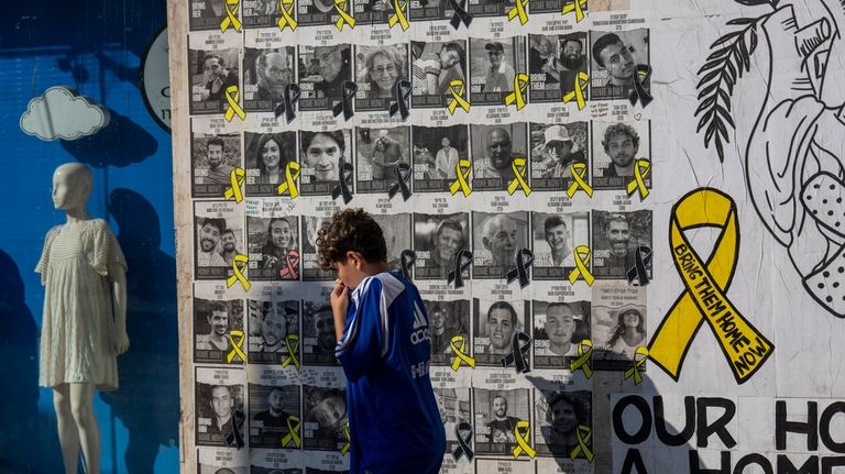 A boy walks past a wall with photos of hostages...