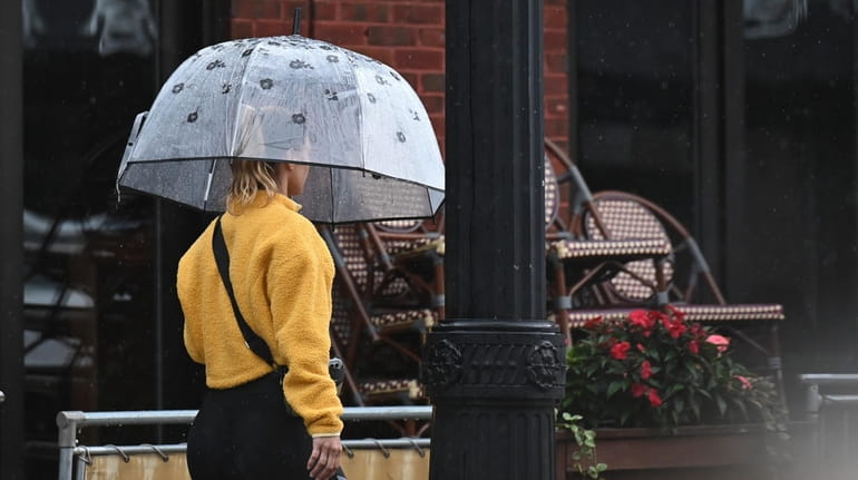 A pedestrian holding an umbrella walks along Main Street in Patchogue as...
