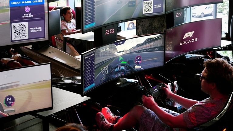 Video game drivers race on a simulated track at the...