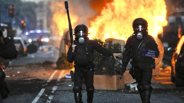 Riot police walk past burning garbage containers during heavy clashes...
