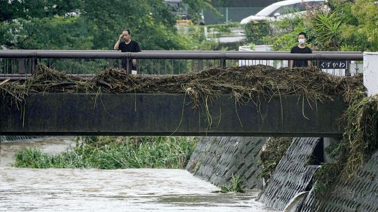 People look at debris stuck on a bridge over a...