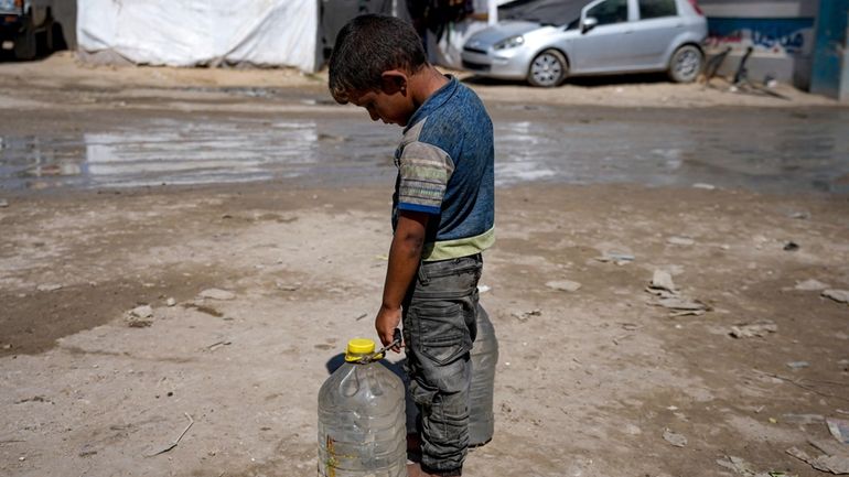 A displaced child carries filled water bottles at a makeshift...