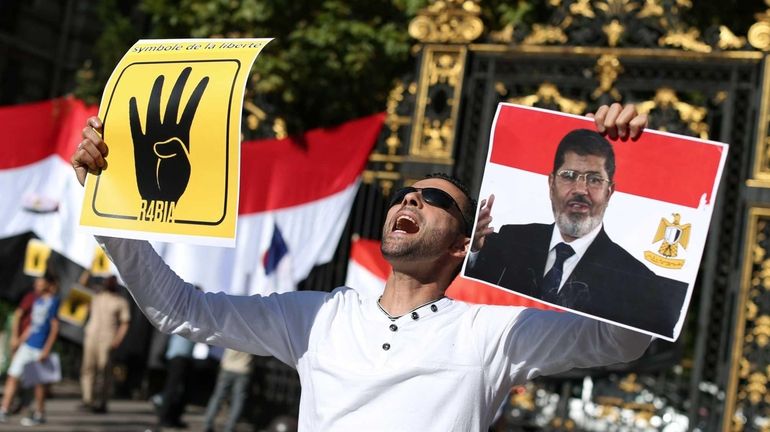 A protester holds a placard reading "R4BIA" and a poster...