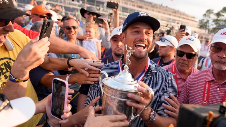 Bryson DeChambeau celebrates with fans and the trophy after winning...