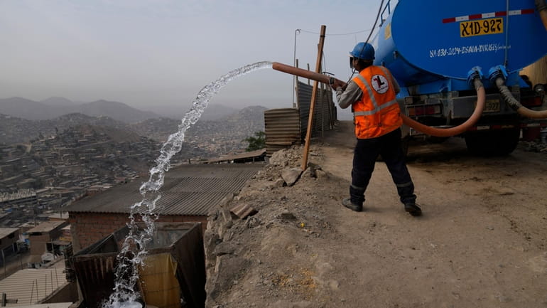 A water truck worker fills a container outside the homes...