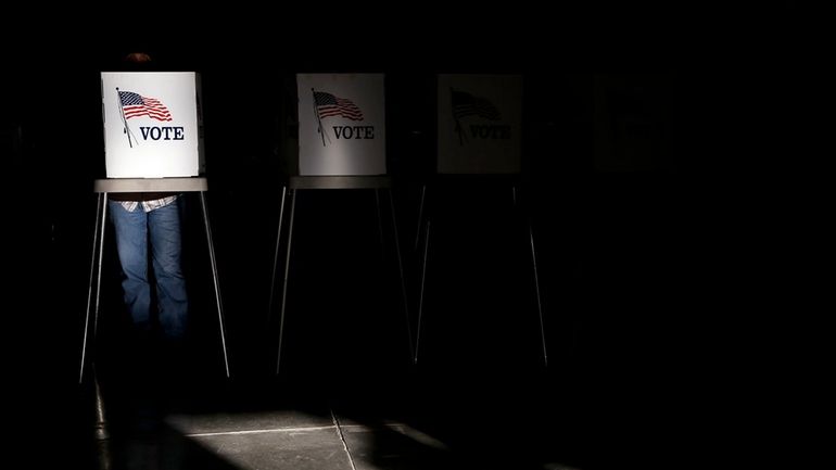 Voting booths are illuminated by a shaft of sunlight as...