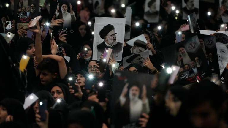Mourners hold up a posters of the late Iranian President...